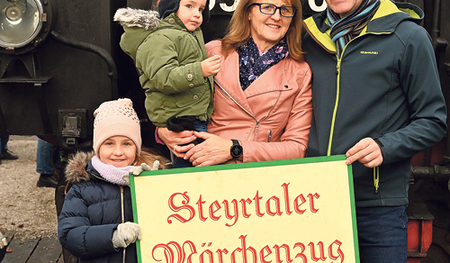 Die Gewinner:innen der Märchenzug-Familienkarte: Lina und Luca mit ihren Großeltern Erna und Karl Reisenberger vor der dampfenden Lokomotive. 